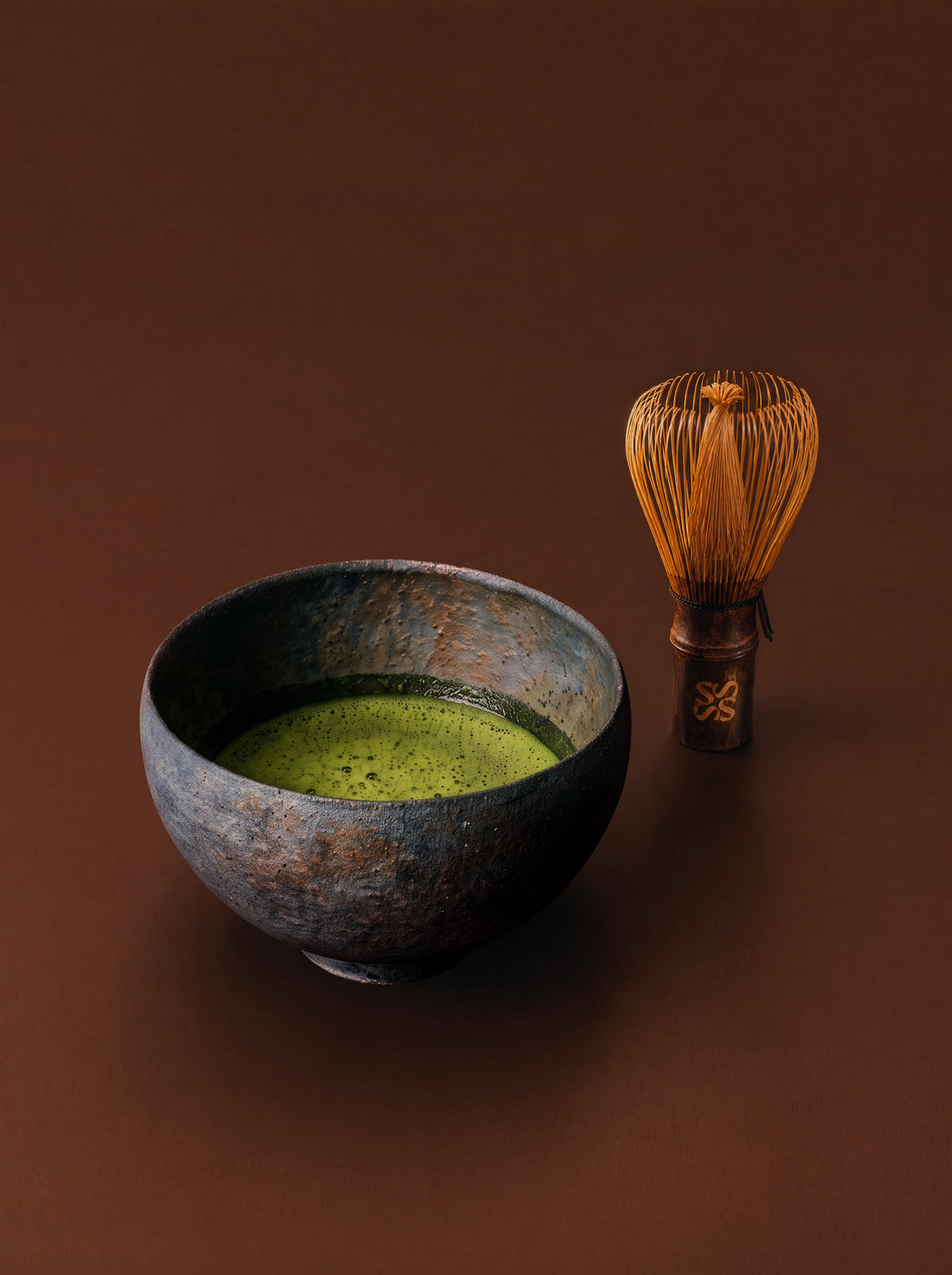 Whisked matcha in a stone bowl beside a bamboo whisk