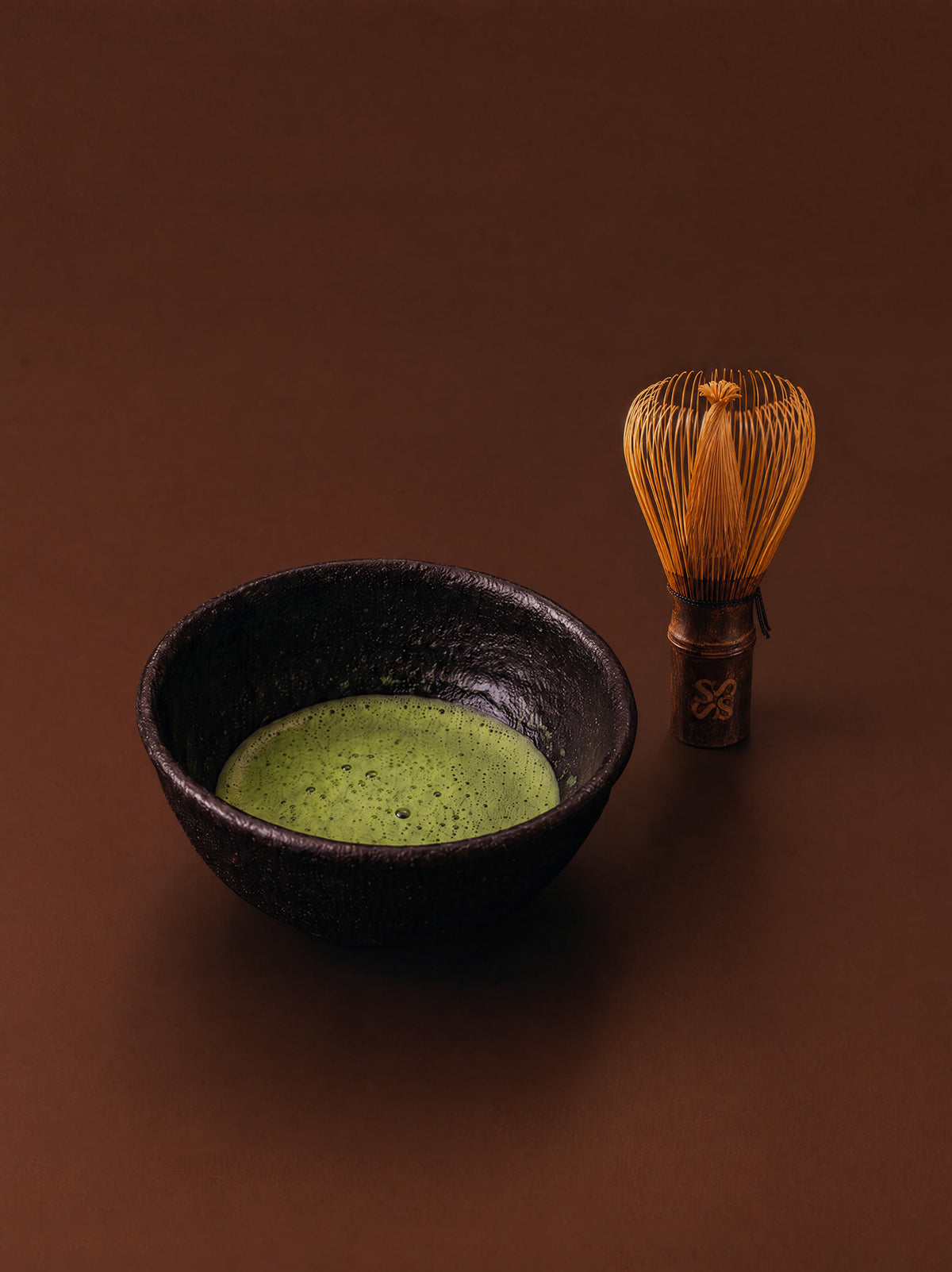 Whisked matcha in a dark bowl beside a bamboo whisk